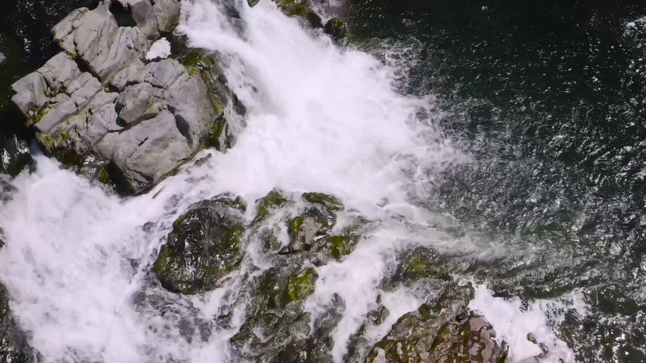 Aerial view of powerful waterfall cascading over rocks, with rushing water below. Top down drone aerial, static establishing shot