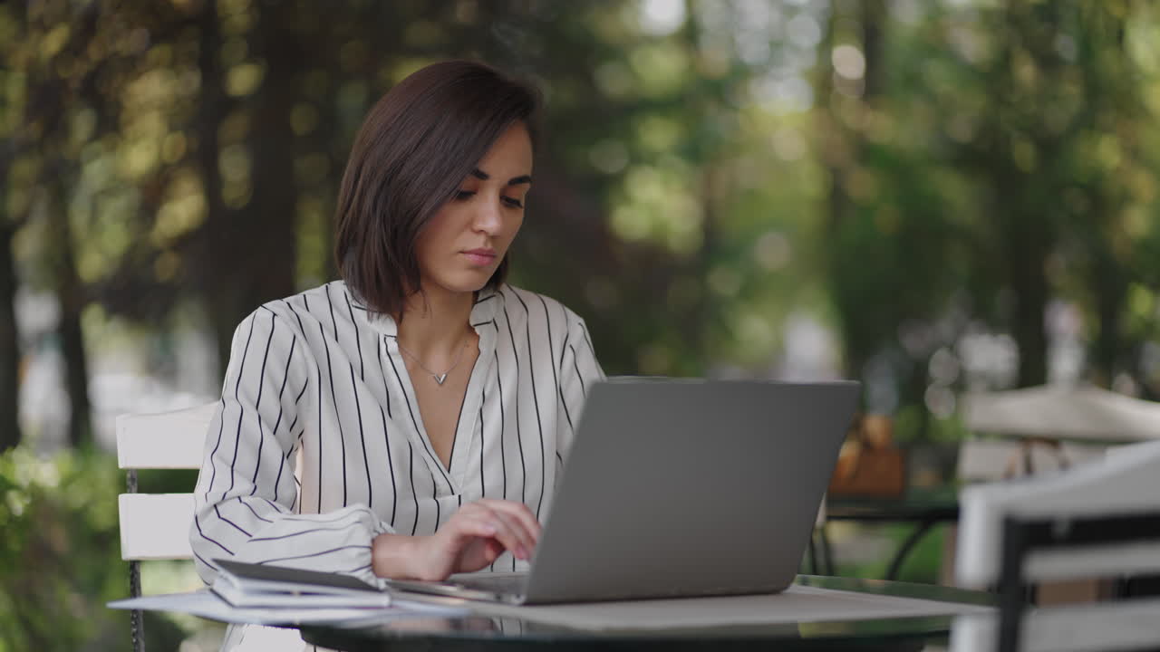 retrato mujer grave morena árabe grupo étnico hispano se sienta en una mesa en un café de verano con una computadora portátil. escribe en el teclado y se somete a capacitación en línea compra y trata con un banco de internet