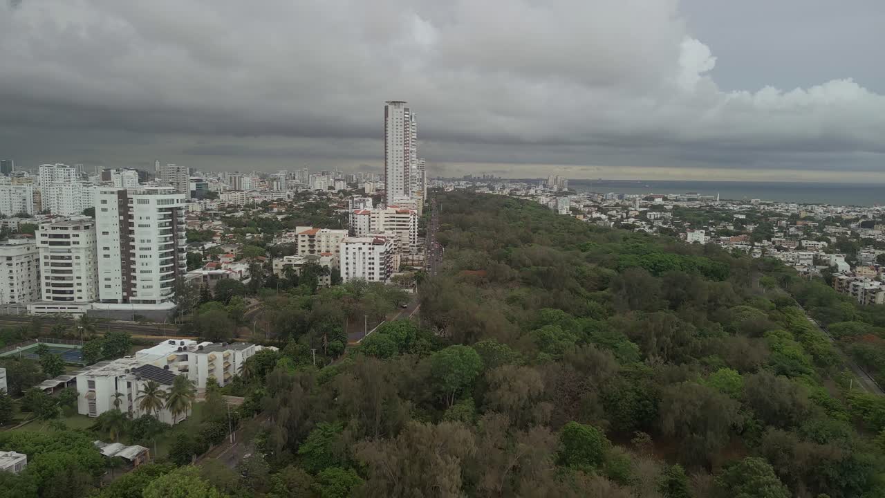 Vista aerea da drone del Parco Mirador Sur che costeggia la città di Santo Domingo. Il verdeggiante parco contrasta con lo skyline urbano sotto un cielo tempestoso. Ideale per i viaggi ai Caraibi e i concetti di vita cittadina.