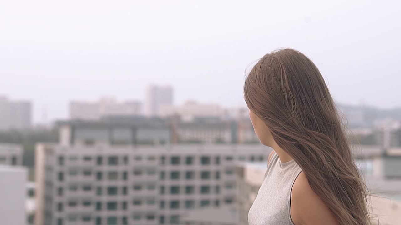 회색 옷을 입은 젊은 여성이 저녁 도시 슬로우 모션을 보고 있습니다.