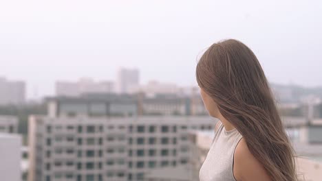 mujer joven con ropa gris mira la ciudad de la tarde en cámara lenta