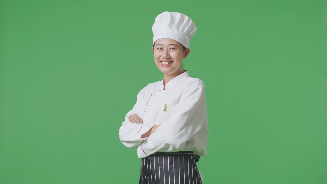 Side View Of Asian Woman Chef Smiling And Crossing Her Arms To Camera While Standing In The Green Screen Background Studio