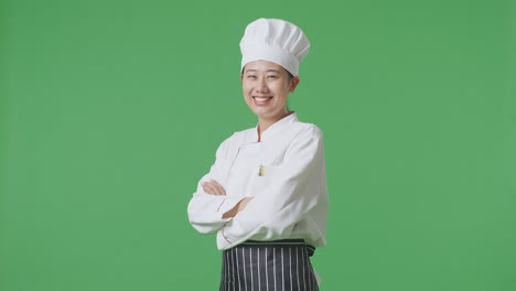 Side View Of Asian Woman Chef Smiling And Crossing Her Arms To Camera While Standing In The Green Screen Background Studio