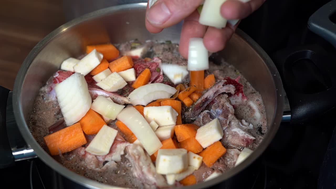 Fresh onions being added to pot of homemade bone broth simmering on stove