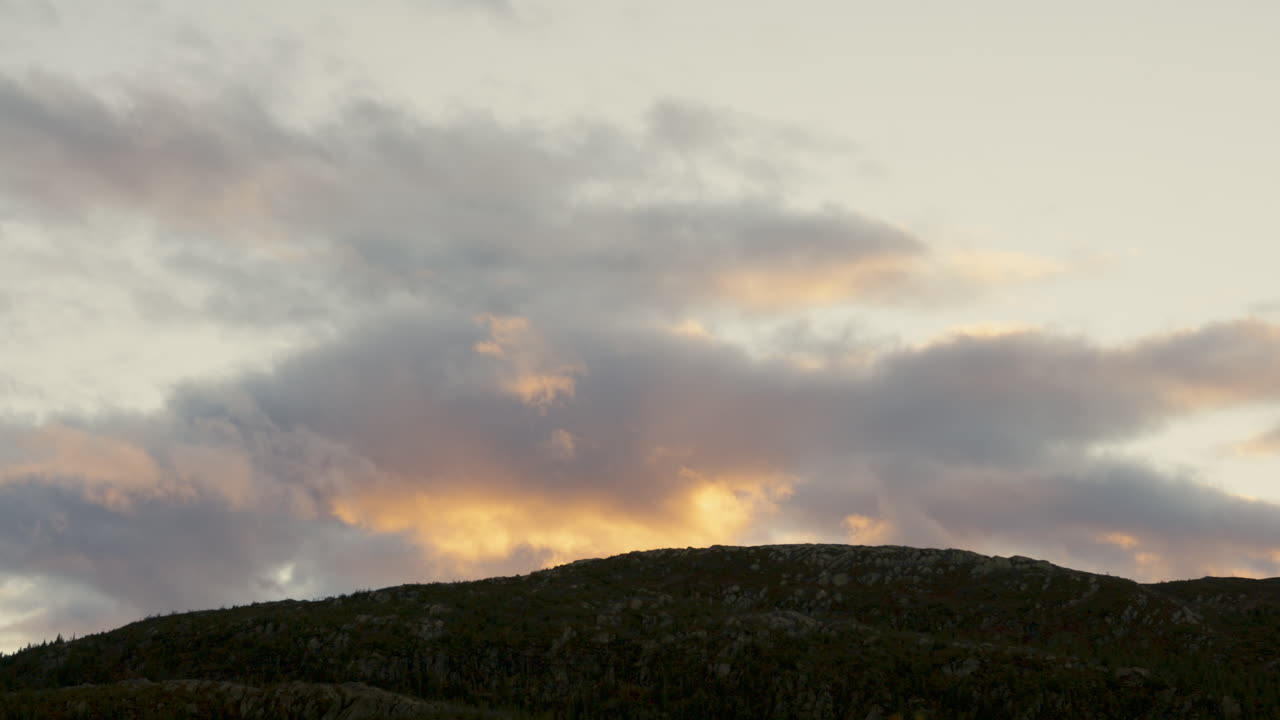 nubes que pasan lentamente por encima de la cima de la montaña al atardecer, coloreadas de amarillo por el sol poniente