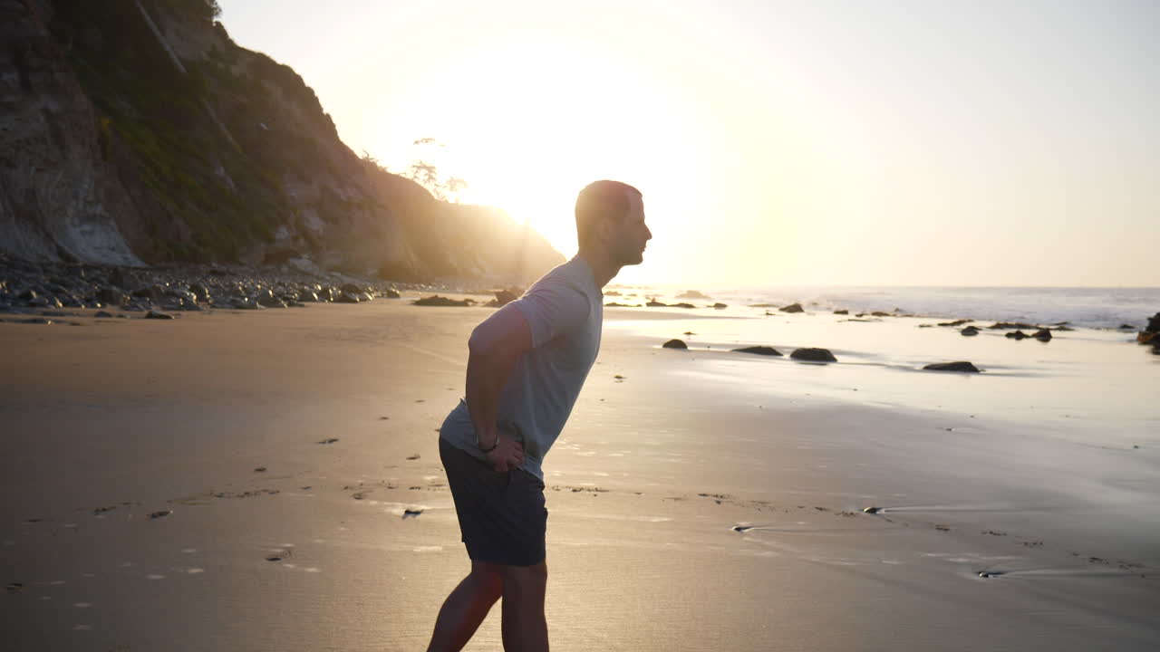 A strong young man stretching his muscles on the beach before a morning fitness workout at sunrise in Santa Barbara, California SLOW MOTION