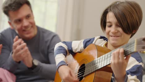 young boy plays classical guitar with an adult watching