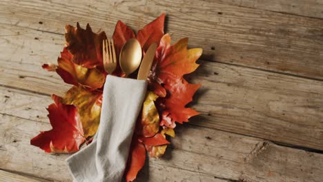 video of cutlery, cloth and autumn decoration with leaves lying on wooden surface