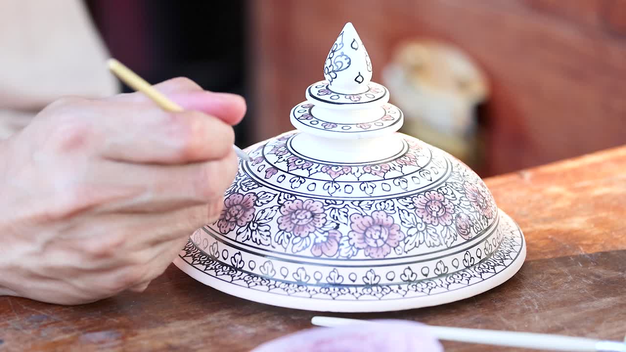 Artista che dipinge con cura motivi intricati su una ciotola di ceramica tradizionale thailandese