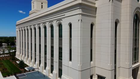 Drone-flying-around-Layton-Temple-that-is-in-construction-close-up-seeing-construction-workers-walking-around-and-taking-break-from-hot-summer-sun,-blue-sky-and-Wasatch-mountain-range-in-background