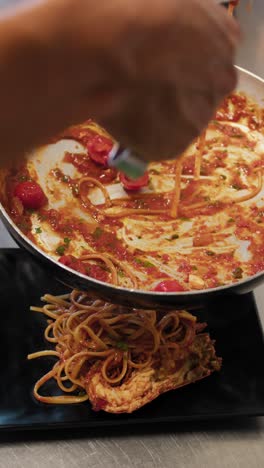 chef using tongs to grab spaghetti from the pan and preparing the final dish