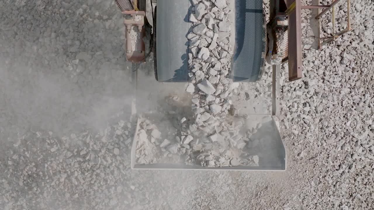 Aerial drone slow motion footage of gravel rocks being dropped off a conveyor belt and falling into a large pile moving to reveal the conveyor belt.