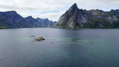 Toma-Aérea-De-Montañas-Escénicas-En-Reinefjorden-En-La-Isla-De-Lofoten-Con-Paddler-De-Pie-En-Un-Agradable-Día-De-Verano