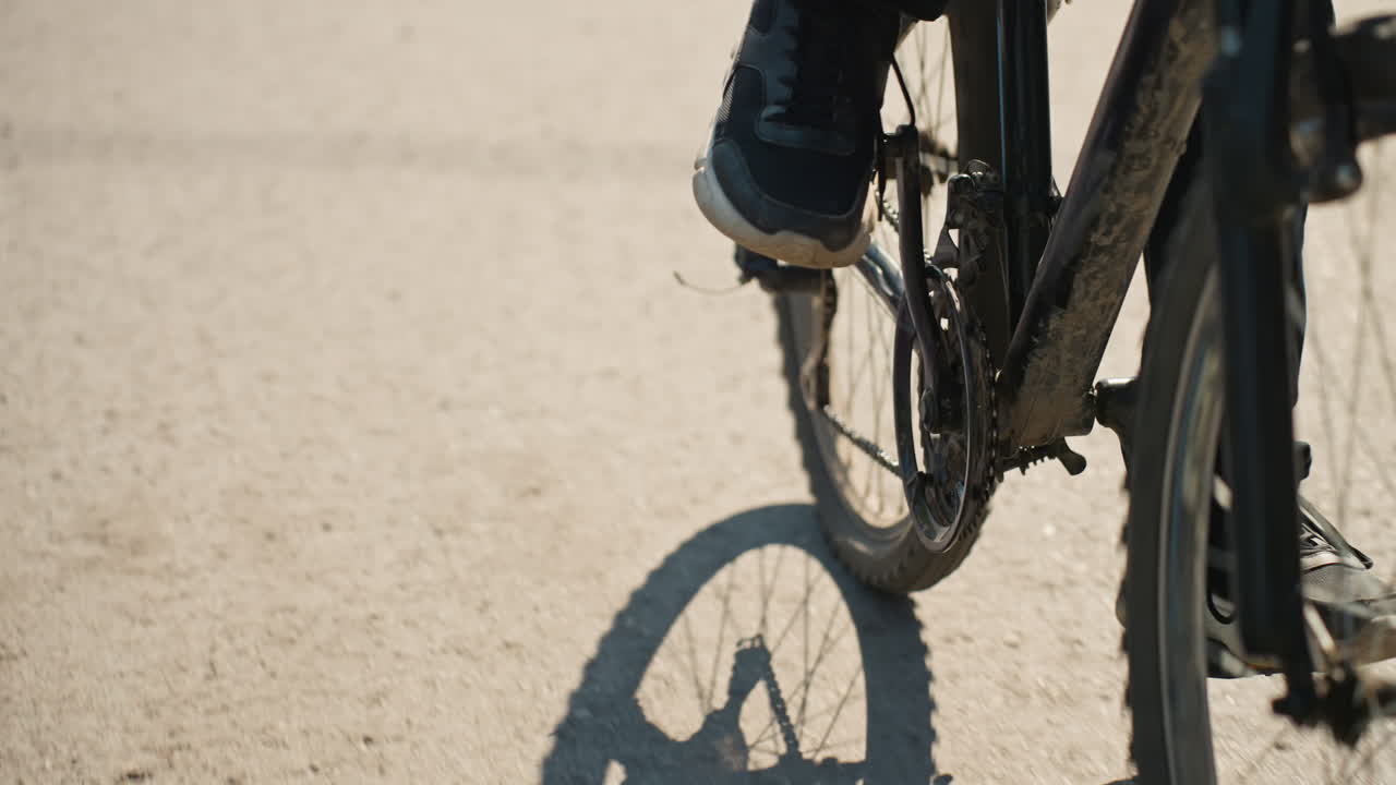 Uomo bianco in bicicletta, primi piani dei pedali sull'asfalto, primi piani dettagliati dei raggi della catena e della trasmissione, scarpe da ginnastica che premono sui pedali, sporco e grasso sul telaio, ritmo di un pendolare concentrato, texture del manto stradale urbano