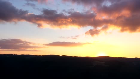 Timelapse-of-sunset-and-red-clouds-disappearing-behind-mountains-in-Black-Forest,-Germany-seen-as-aerial-view-in-4k