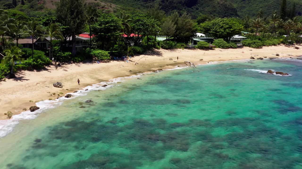 4K drone footage of a stunning tropical beach in Kauai. Vibrant reef, turquoise water, and dramatic mountain backdrops create the perfect Hawaiian travel or nature scene