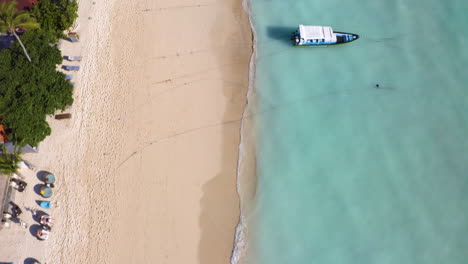 Nusa-Lembogan-sunset-beach-in-Bali-Indonesia,-bird's-eye-view-tilting-the-drone-to-film-4k-footage-of-beautiful-sandy-beach-with-clear-ocean-and-sailing-boats