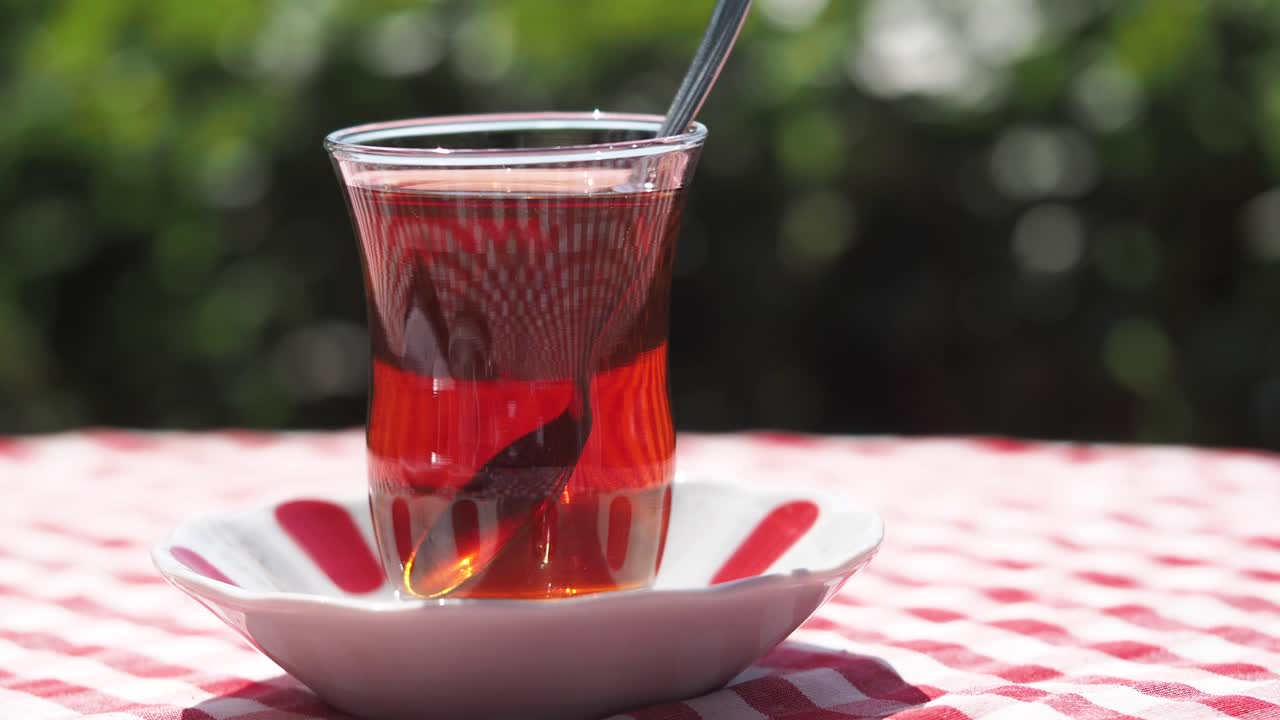 A glass of Turkish tea on a red and white checkered tablecloth outdoors