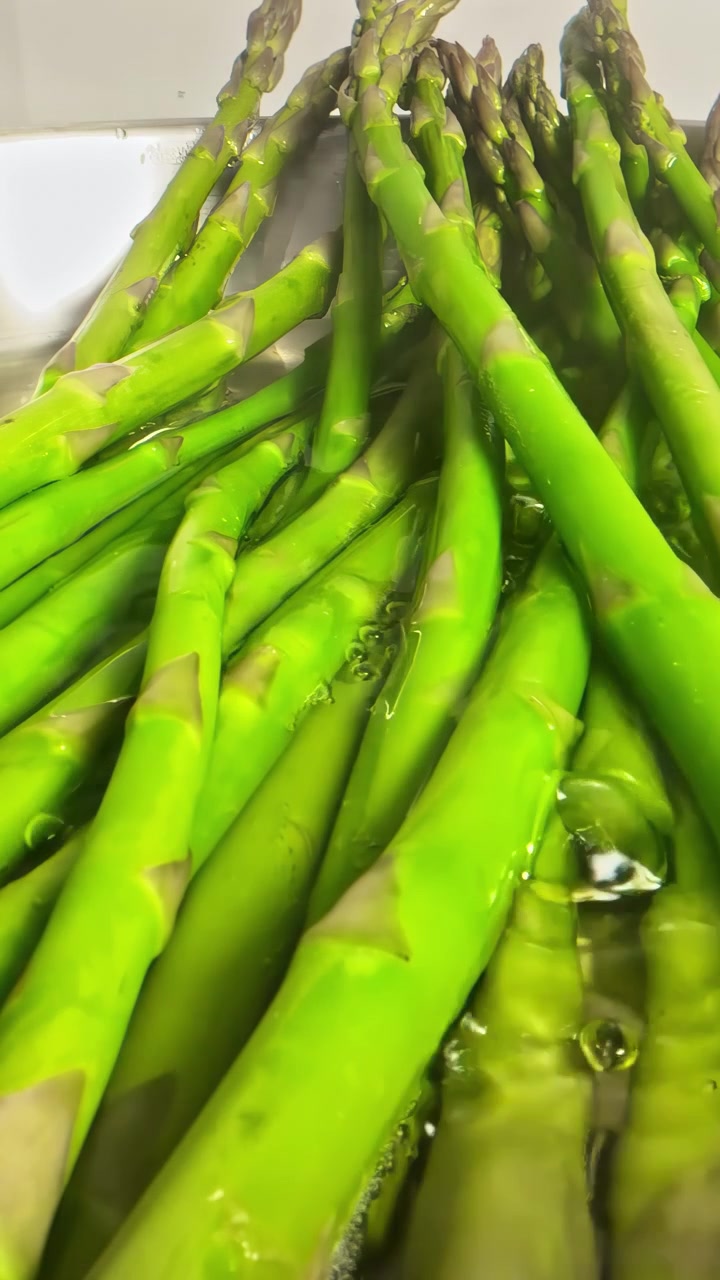 A close-up of vibrant green asparagus spears soaking in water. Perfect for culinary blogs or cooking tutorials focusing on fresh produce preparation.