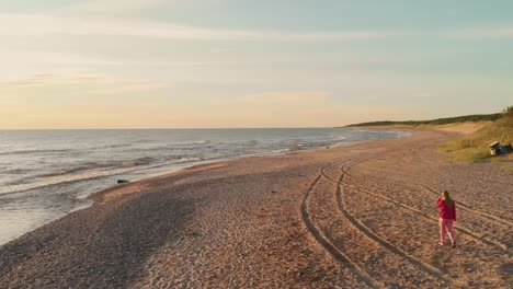 Young-woman-walking-on-Baltic-sea-coastline-during-golden-sunset