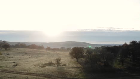 An-aerial-drone-shot-over-a-misty-land,-flying-towards-the-son-over-hills-and-forest