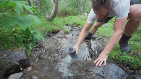 excursionista masculino obtiene agua potable de un río de montaña limpio en noruega