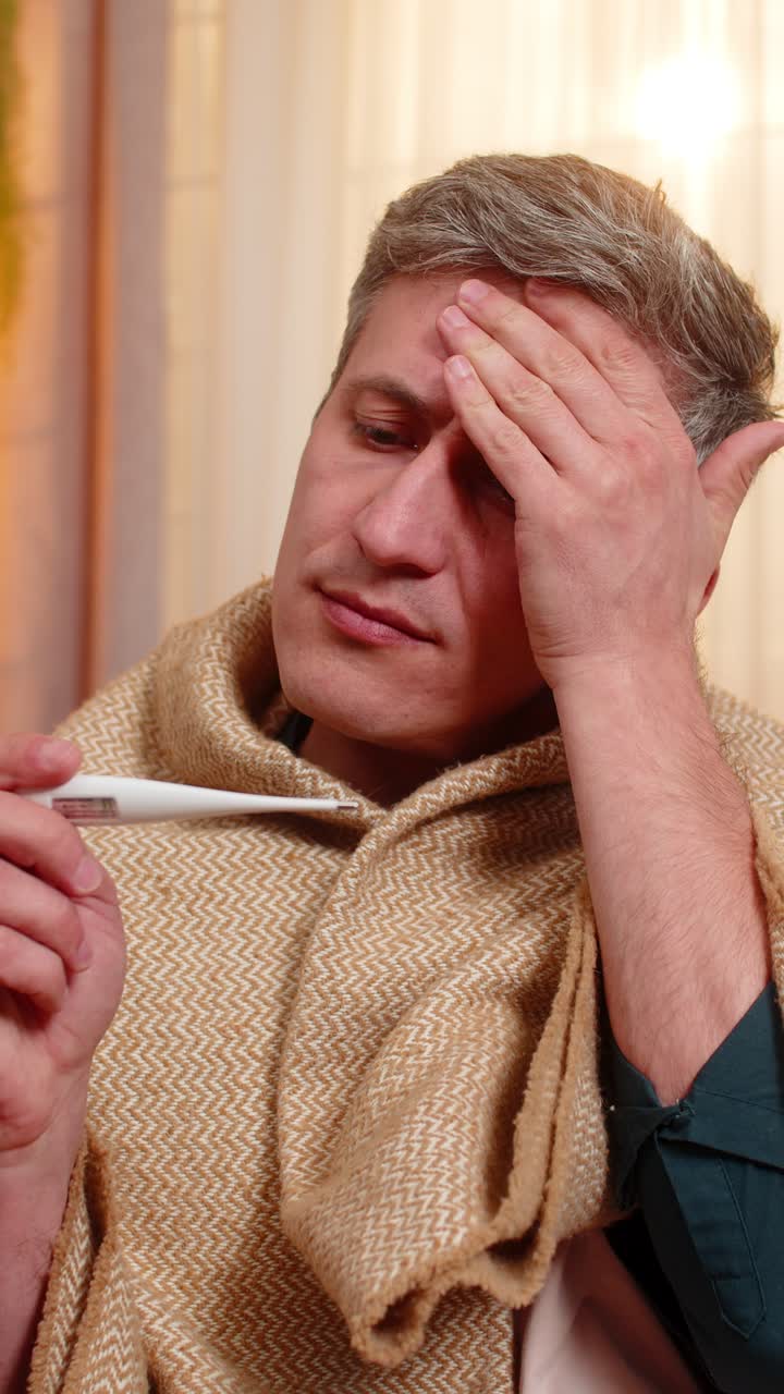 Young man checks body temperature with thermometer looks worried about possible illness and fever