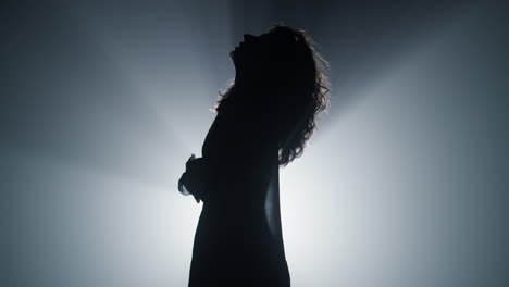 Silhouette-girl-moving-hands-in-air-indoors.-Attractive-woman-looking-up-in-dark