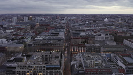 Forwards-fly-above-evening-city.-Blocks-of-buildings-and-streets-at-dusk.-Vehicles-driving-on-roads.-Berlin,-Germany