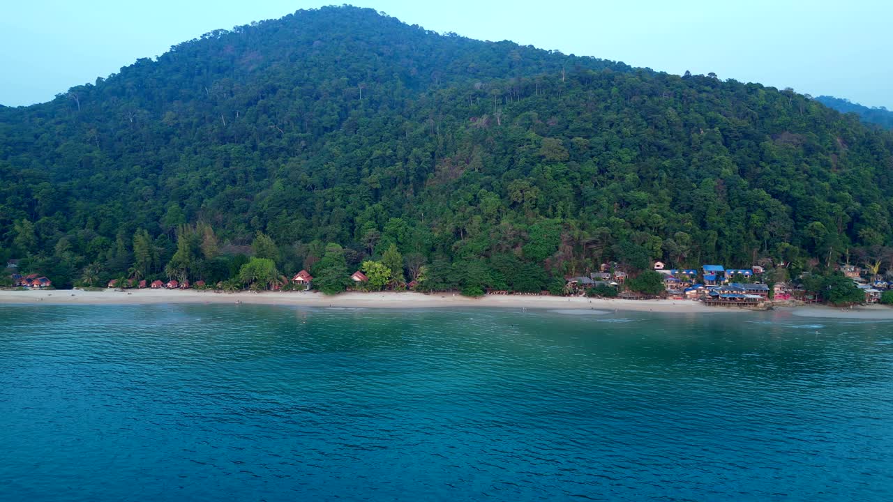 Koh Chang Tropical beach with bungalows along the shore and dense green jungle covering a mountain. Best aerial view panorama overview drone