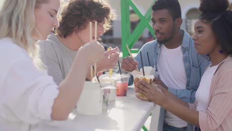 group of cheerful  friends eating street food in the city while chatting and having fun together