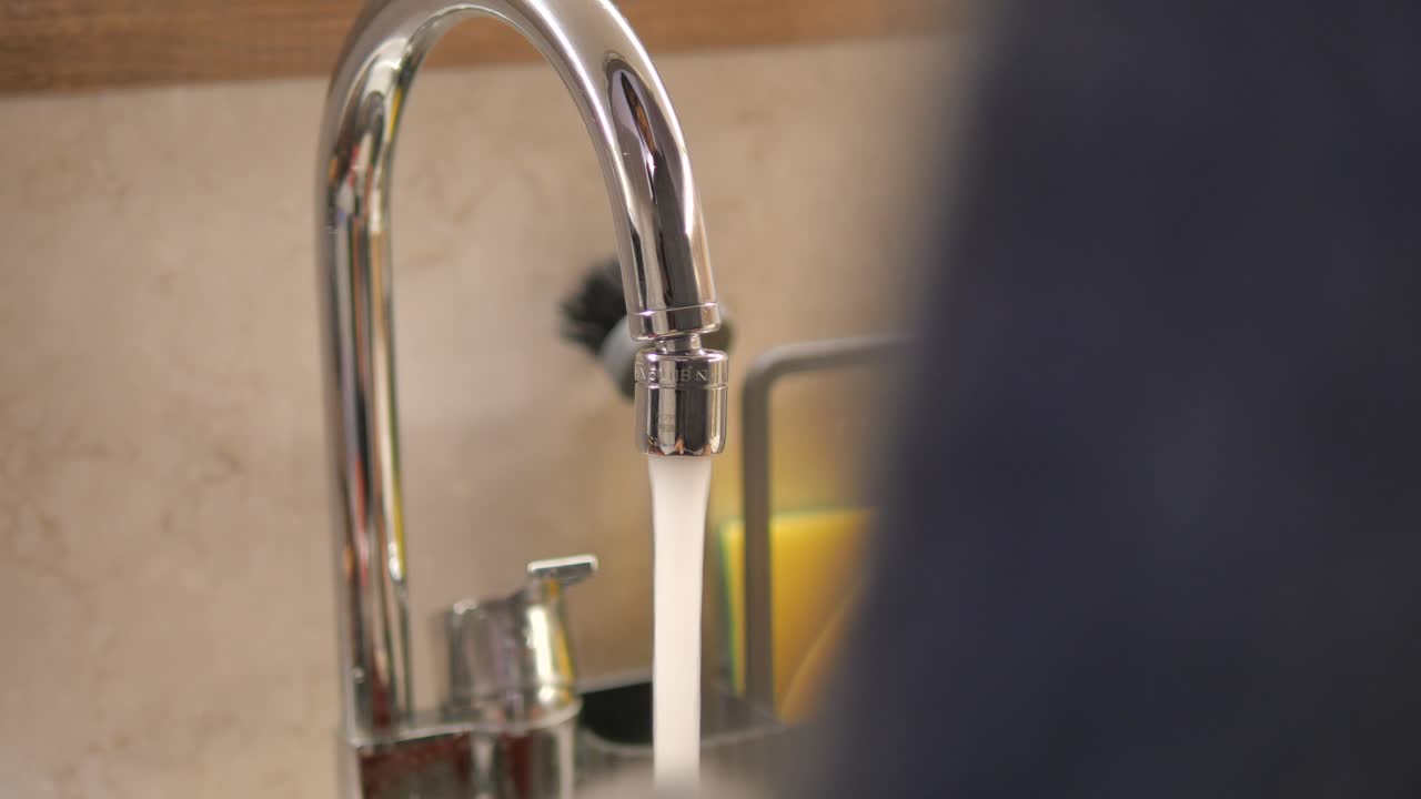 Primo piano di un rubinetto da cucina cromato con acqua che scorre