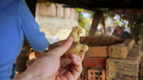 A-close-up-of-a-traditional-clay-flute-from-Thanh-Ha,-Vietnam,-with-an-ape-on-top,-a-perfect-souvenir-for-tourists,-showcasing-all-angles-in-hand