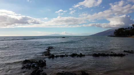 rocky beach view of the surf with clouds overhead and lanai island and the west maui mountains in the background near kihei maui hawaii.
