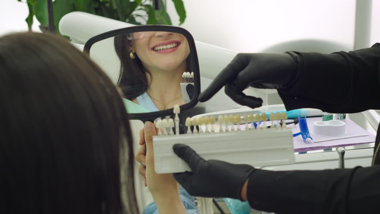 Smiling woman choosing dental veneer shade at clinic, guided by dentist