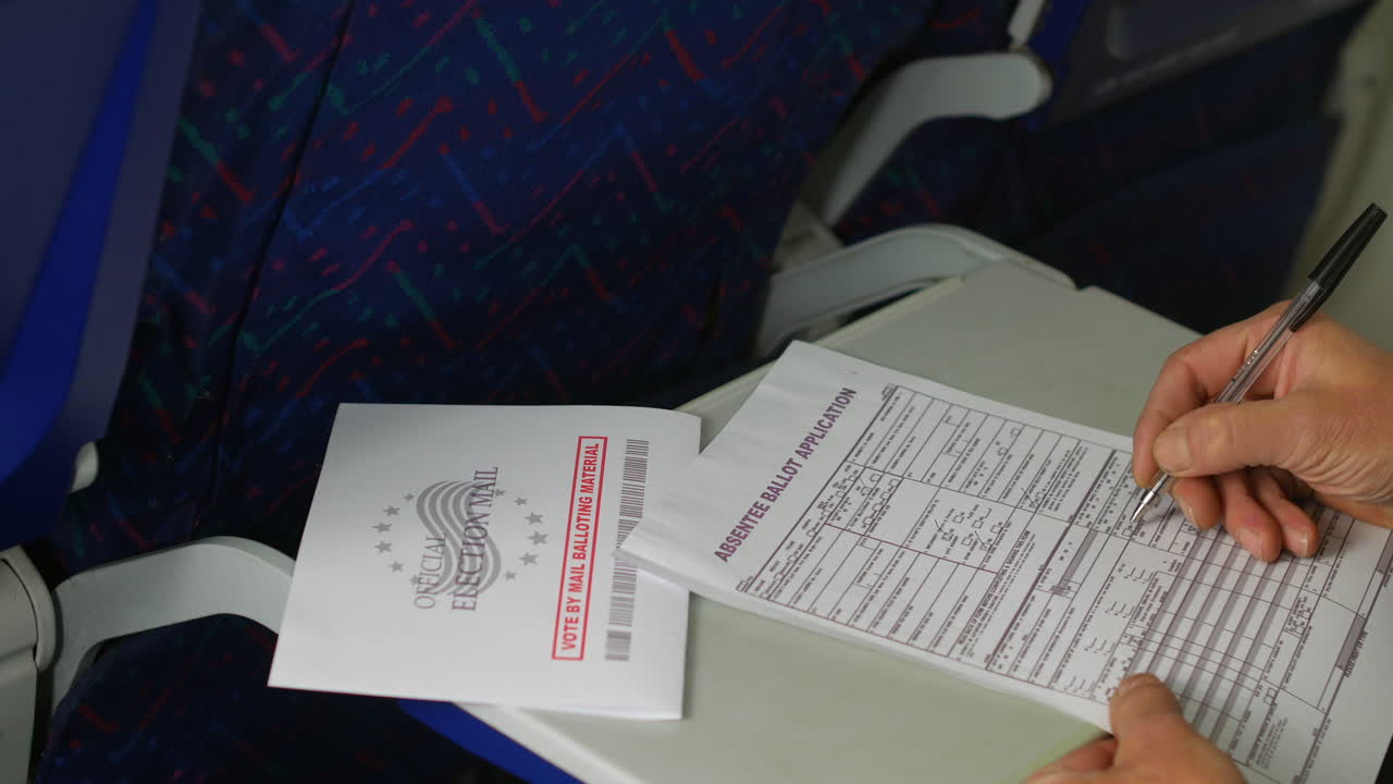 Completing an absentee ballot application on an airplane tray table. The "Official Election Mail" envelope rests nearby, emphasizing the convenience of voting by mail while traveling.