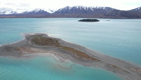 sandy beach in lake tekapo with motuariki island in the distance in south island, new zealand. - aerial pullback shot