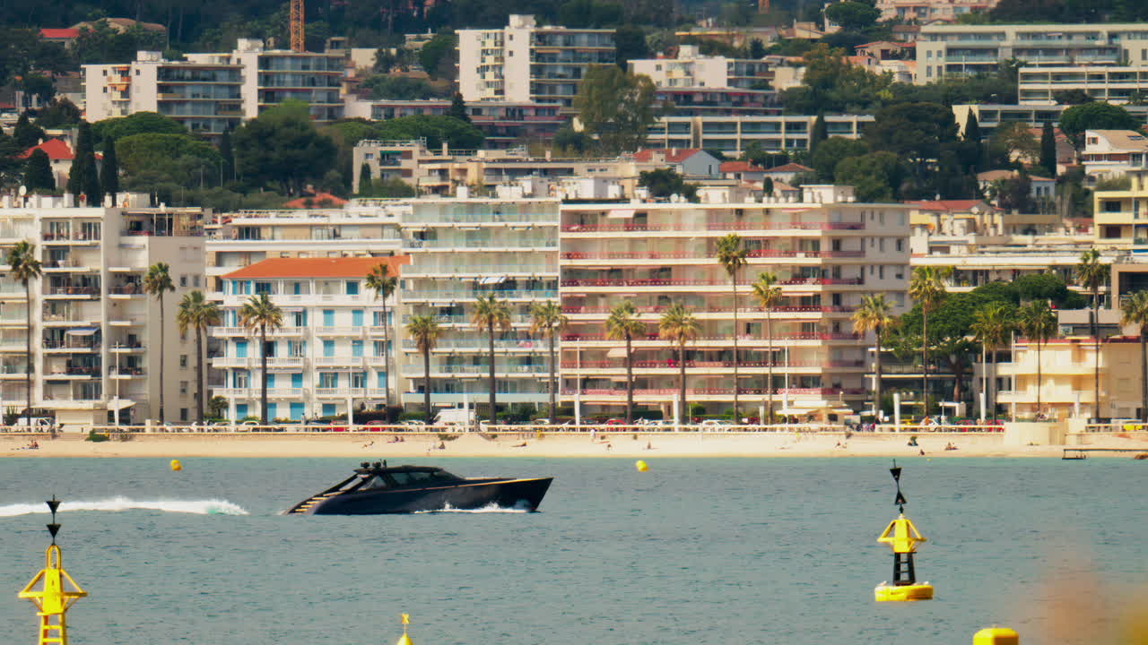 Boat moving on the sea in Juan-les-Pins, France with the beach and the buildings on the background