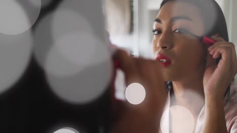 animation of light spots over biracial woman applying mascara