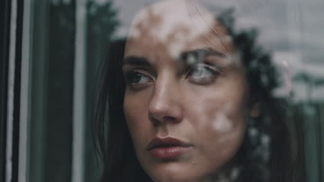 pensive woman looking through a window with reflections