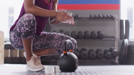 Video-Des-Unteren-Teils-Einer-Afroamerikanischen-Frau,-Die-Sich-Die-Hände-Pudert,-Bevor-Sie-Im-Fitnessstudio-Kettlebell-Hebt