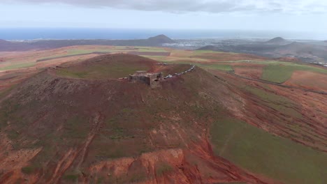 Ziehen-Sie-Die-Drohnenaufnahme-Einer-Burg-Am-Rand-Eines-Roten-Vulkans-Zurück