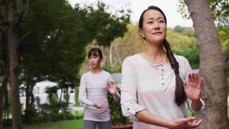 happy asian mother exercising in garden with daughter, practicing tai chi together