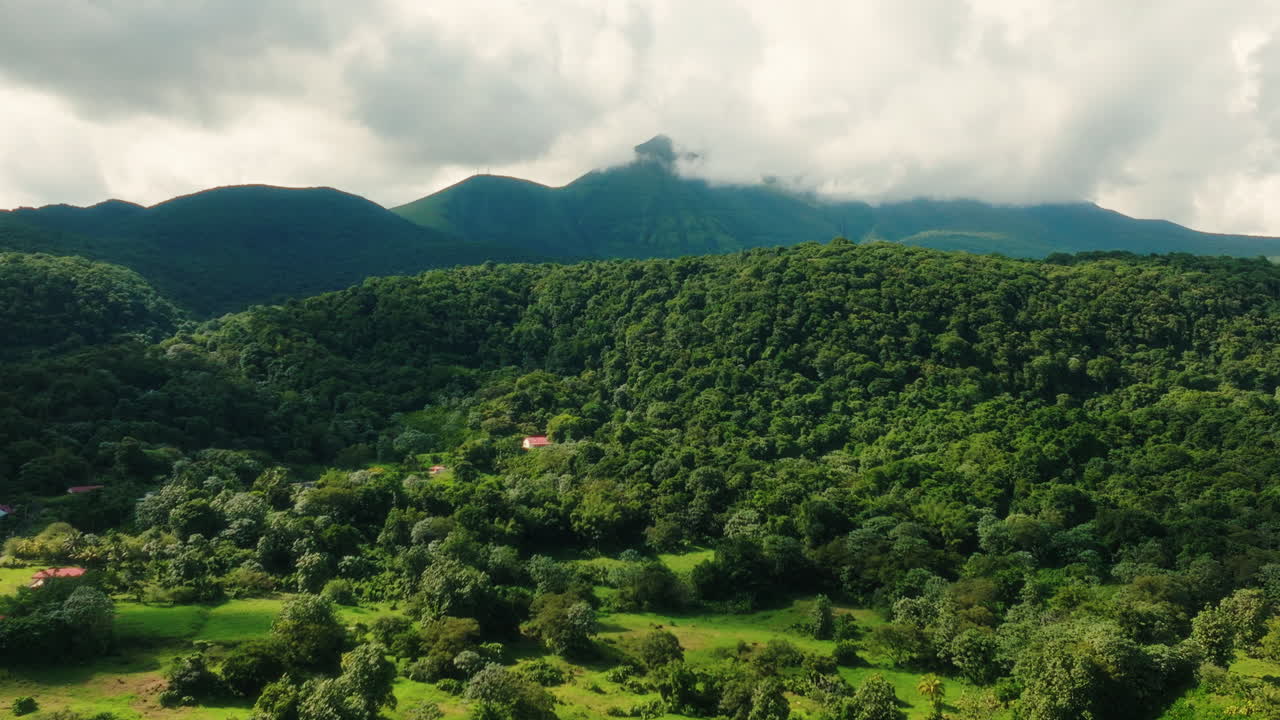 Drone ascends and pans left to right over lush tropical forest and mountains covered with clouds in Guadeloupe