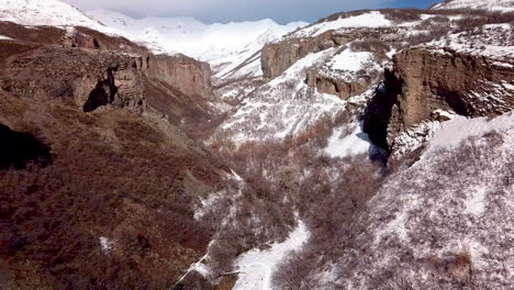 flying above a hiking trail at the bottom of a rugged canyon with cliffs all around during winter