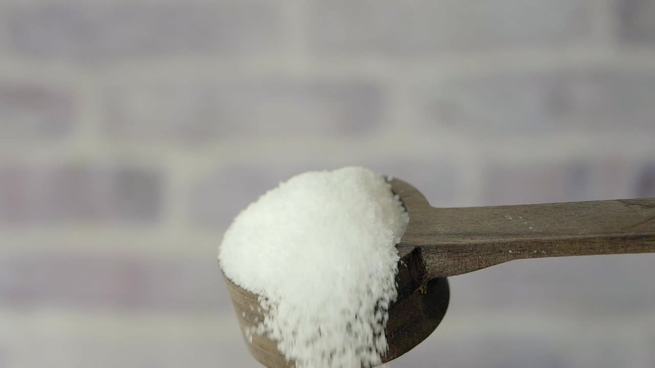 cerca de una cuchara de madera llena de azúcar granulado blanco