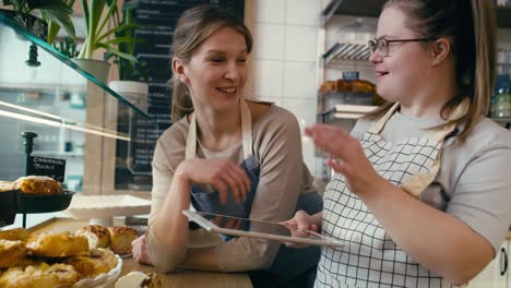 down syndrome girl and her female workmate using digital tablet to check the commodity of the bakery