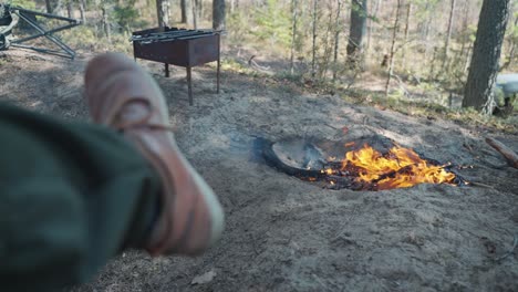 tourist sits by a fire in a forest camp, first-person view. the concept of outdoor recreation.