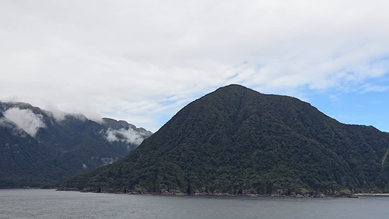 Milford Sound, Fiordland National Park, New Zealand dramatic fjord landscape with steep forested peaks, mist clad summits and calm reflective waters under moody clouds