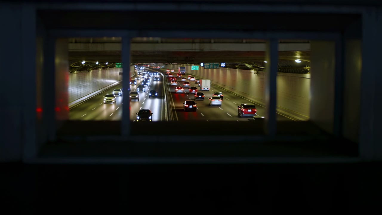 En travel urban motorveiscene om natten, som viser dynamisk trafikkflyt med flere kjørefelt og tunneler. Kjøretøy beveger seg jevnt gjennom betong- og metallstrukturer, opplyst av sterkt